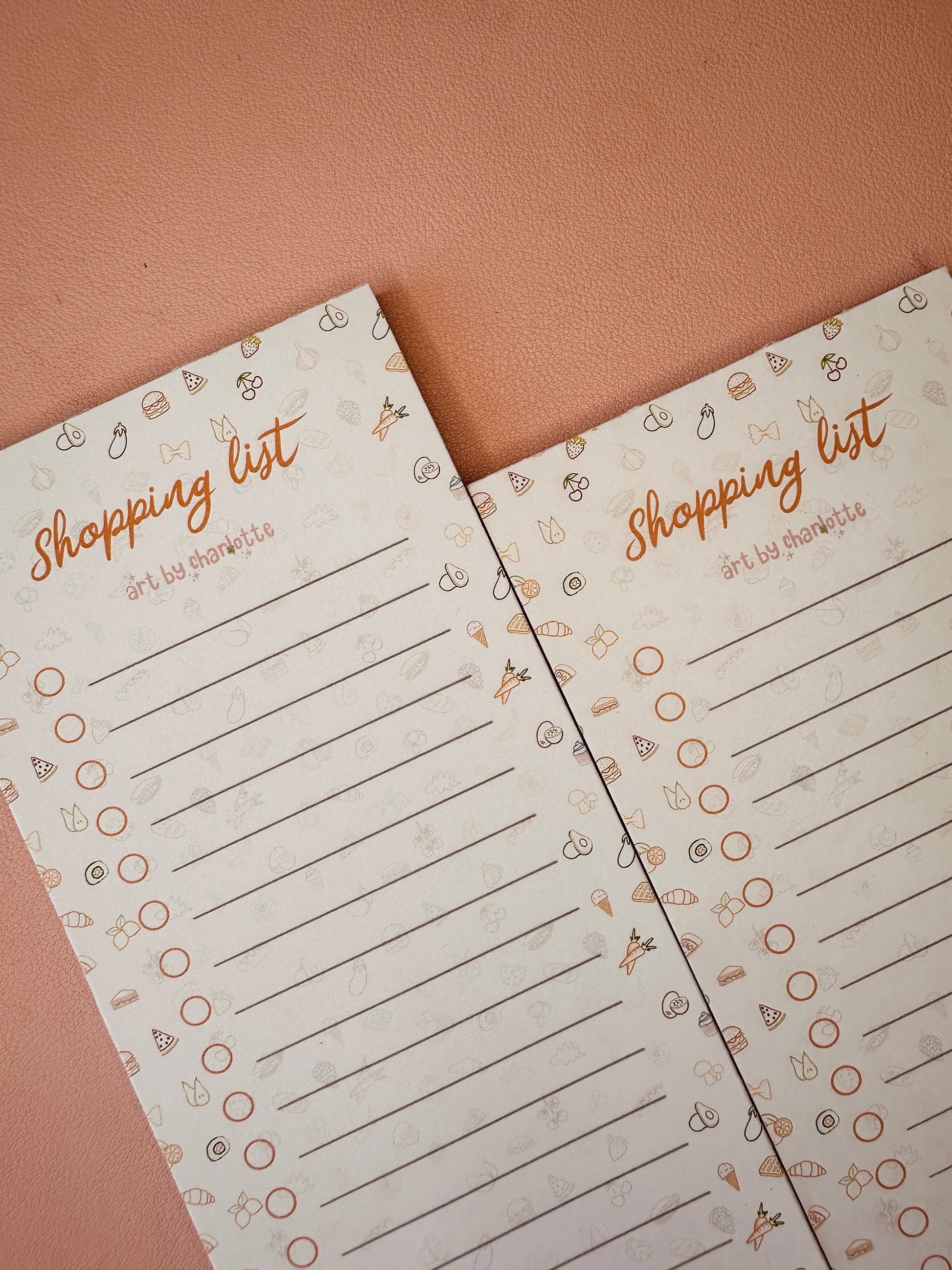 Two shopping list pads with decorative elements on a brown background