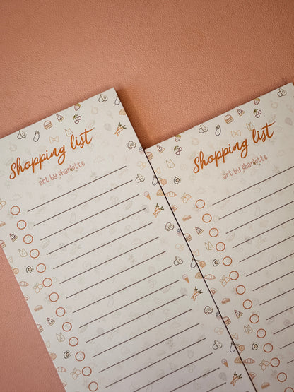 Two shopping list pads with decorative elements on a brown background