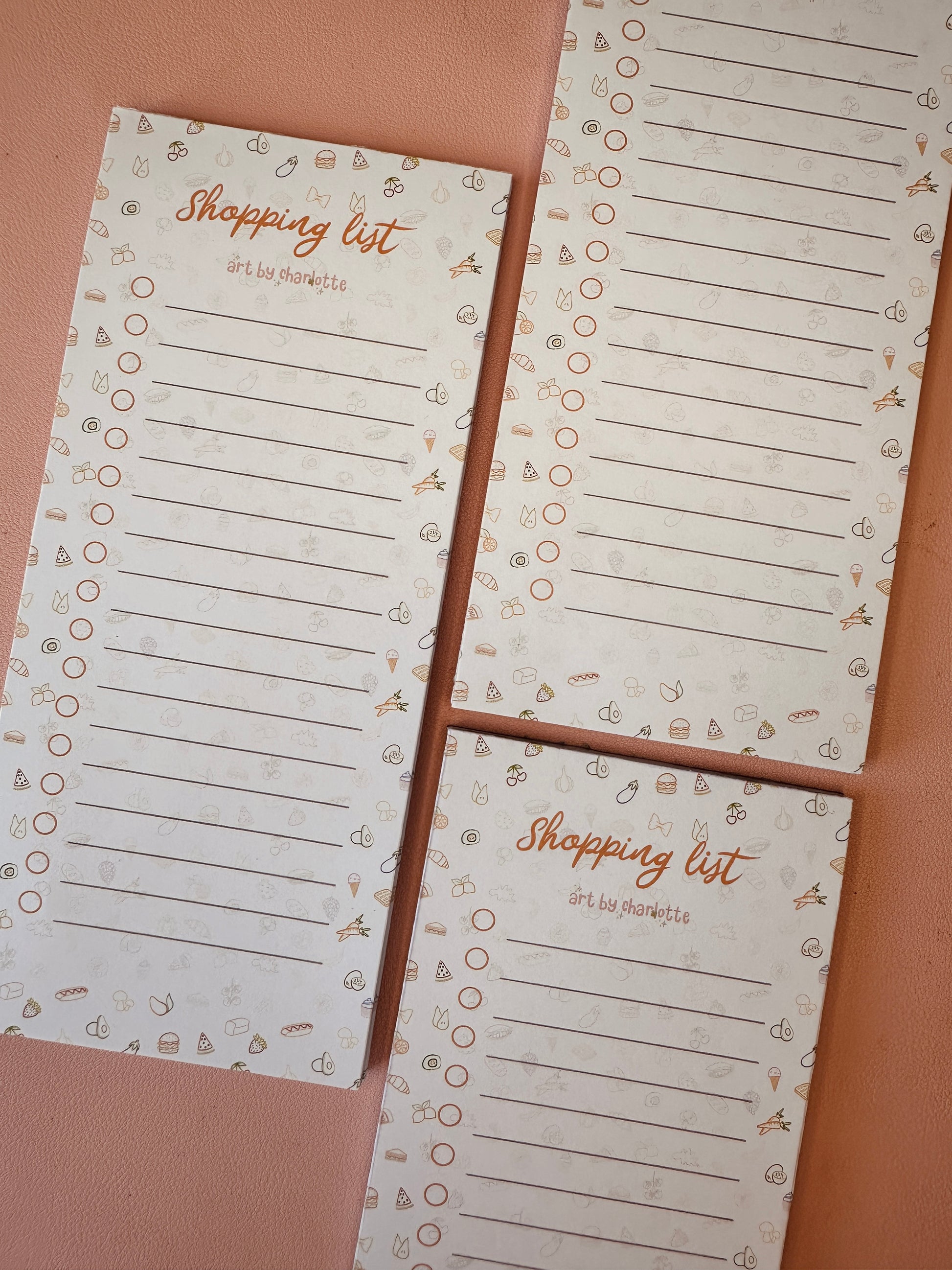 Set of three shopping list pads with decorative elements on a brown background