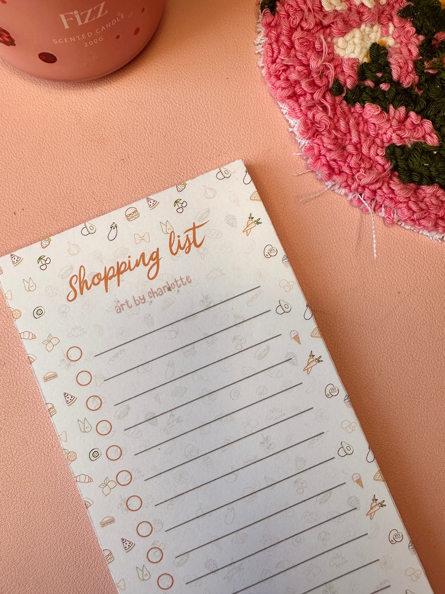 Shopping list pad with decorative elements on a pink surface