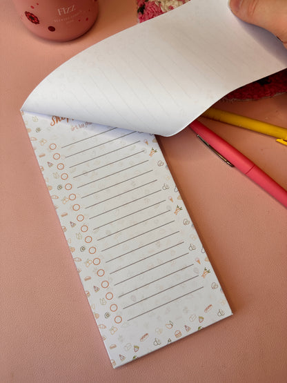 Notebook with lined pages and decorative border on a pink surface with pens.
