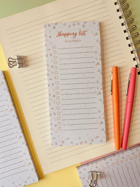 Notepad with 'Shopping list' on a desk with two pens
