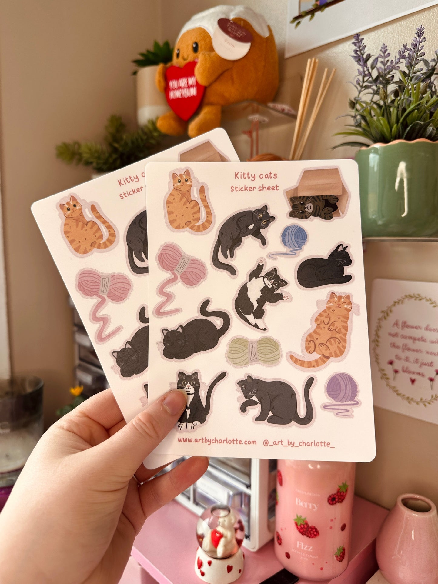 Sticker sheet with cat designs held by a hand in a casual indoor setting.